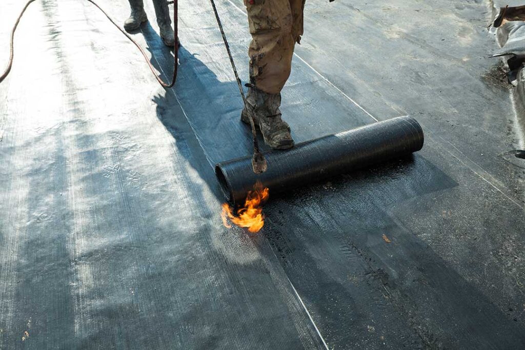 A person standing on a ladder gently scrubbing green moss off a shingle roof with a soft brush.