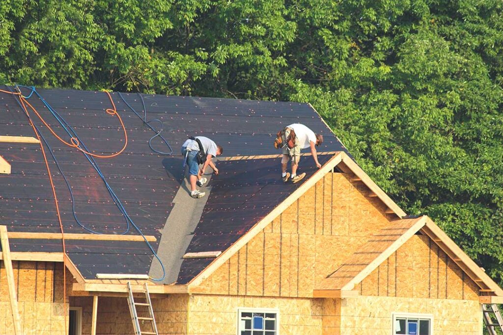 A worker in a safety harness installs solar panels on a residential asphalt shingle roof.