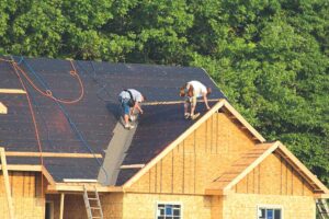 A worker in a safety harness installs solar panels on a residential asphalt shingle roof.
