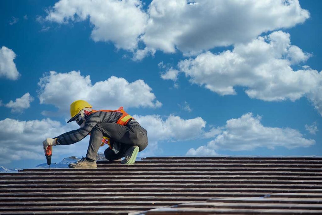 Workers sort old asphalt shingles, metal flashing, and roofing paper into separate covered containers.