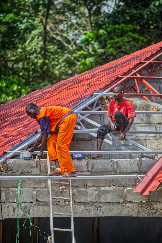 Workers inspect a protected residential roof beside ladders, covered materials, gutters, and renovation tools.